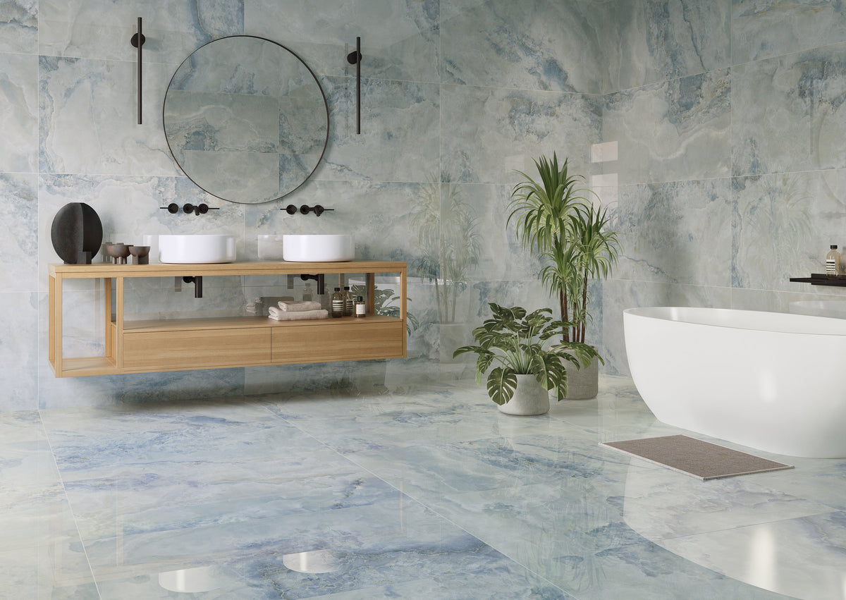 A modern bathroom interior with blue-gray marble-look tiles, a floating light wood double-sink vanity, a round wall mirror, a