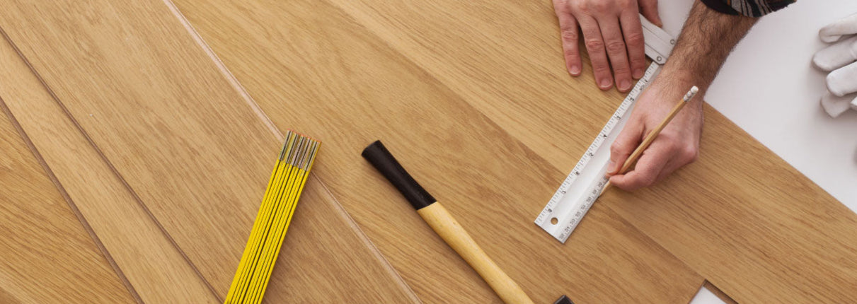 Installer measuring wooden flooring with tools on a wooden surface