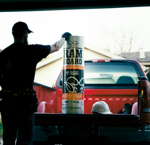 A person in a black shirt and cap stands in the bed of a red pickup truck holding a large