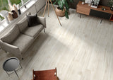 Wood-look porcelain floor tiles installed in a modern living room setting with a gray sofa, wooden sideboard, and plants.