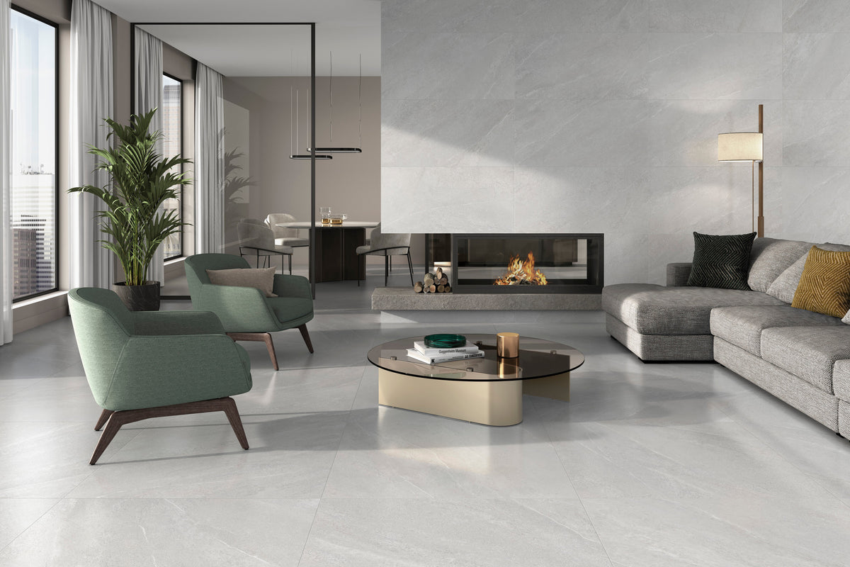 A modern living room with light gray stone-look porcelain floor tiles, featuring a gray sectional sofa, two green accent chai