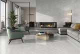 A modern living room with light gray stone-look porcelain floor tiles, featuring a gray sectional sofa, two green accent chai