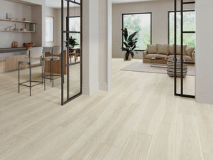 Light beige wood-look tile plank flooring shown in a modern, bright open-plan living space with a kitchen, sofa, and black-fr
