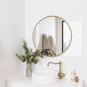 Bathroom with round gold mirror, white subway tiles, white sink, and greenery.