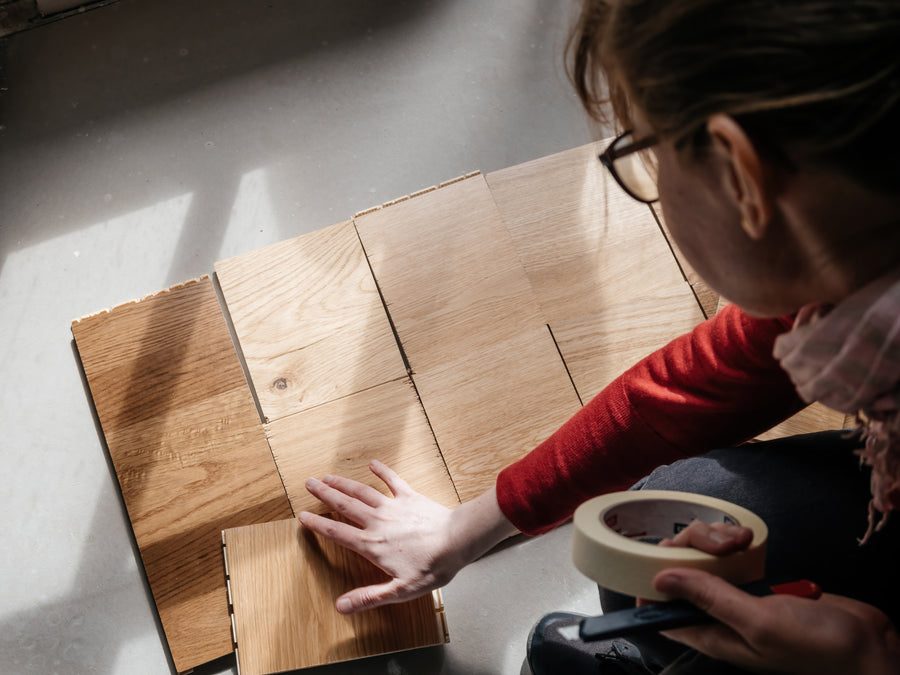 Oak plank samples laid out on a bare floor in direct sunlight, held in place with masking tape, being compared before a decision
